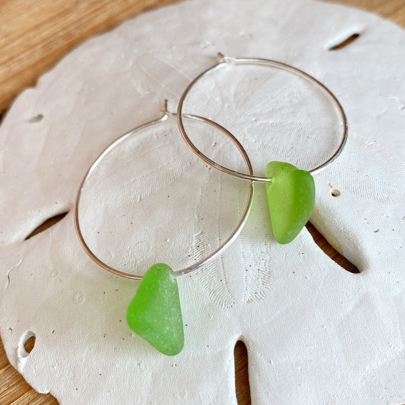 Green sea glass earrings on a sand dollar with a wooden background