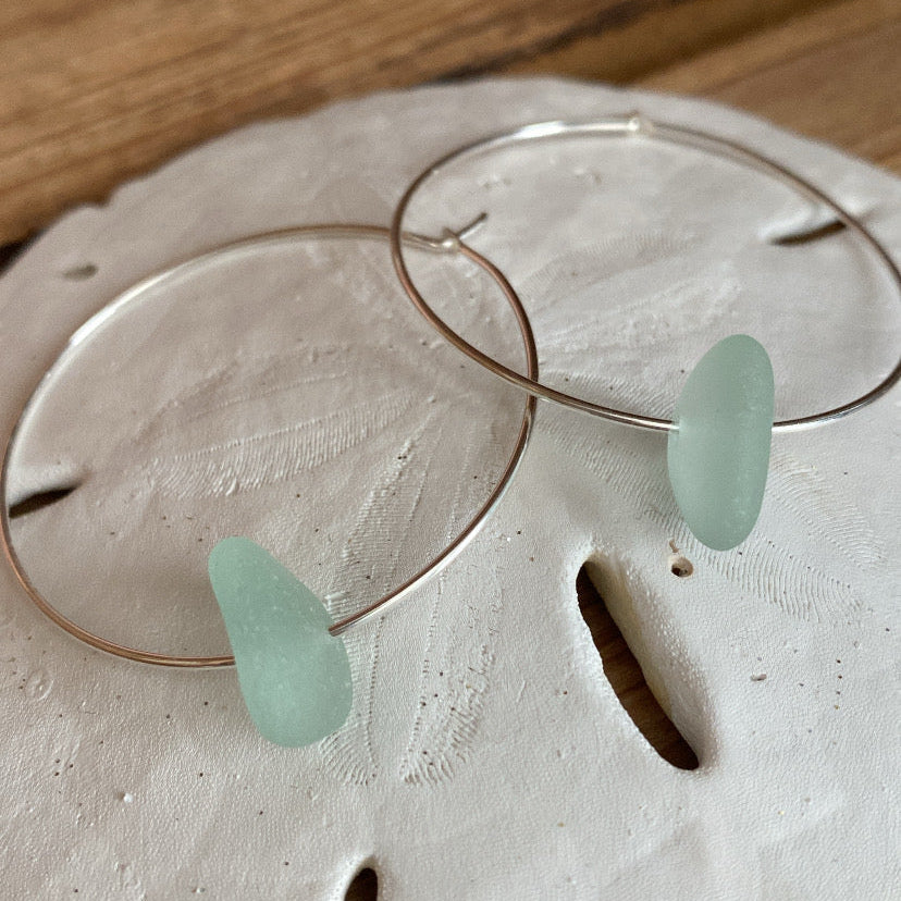 Silver hoop earrings with sea glass on a sand dollar