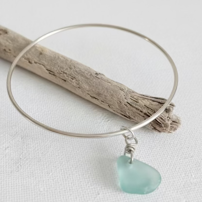 Silver bangle with a sea glass charm on a white fabric background