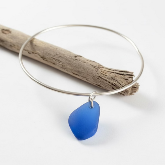 Silver bangle with a blue sea glass charm on a neutral background