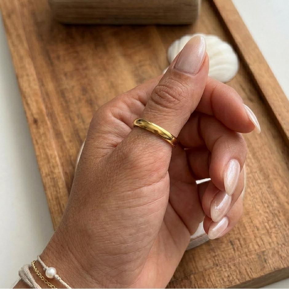 Hand wearing a gold ring on a wooden surface with a white background