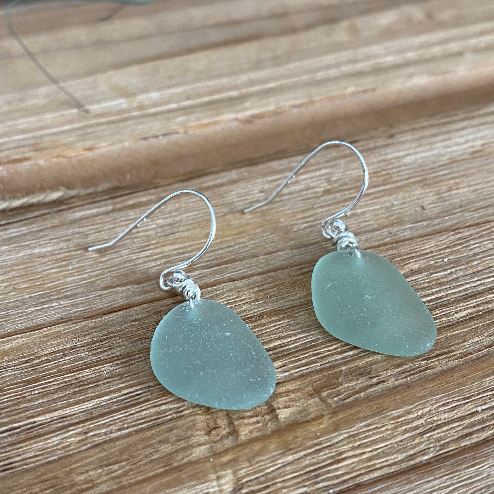 Pair of light blue sea glass earrings on a wooden surface