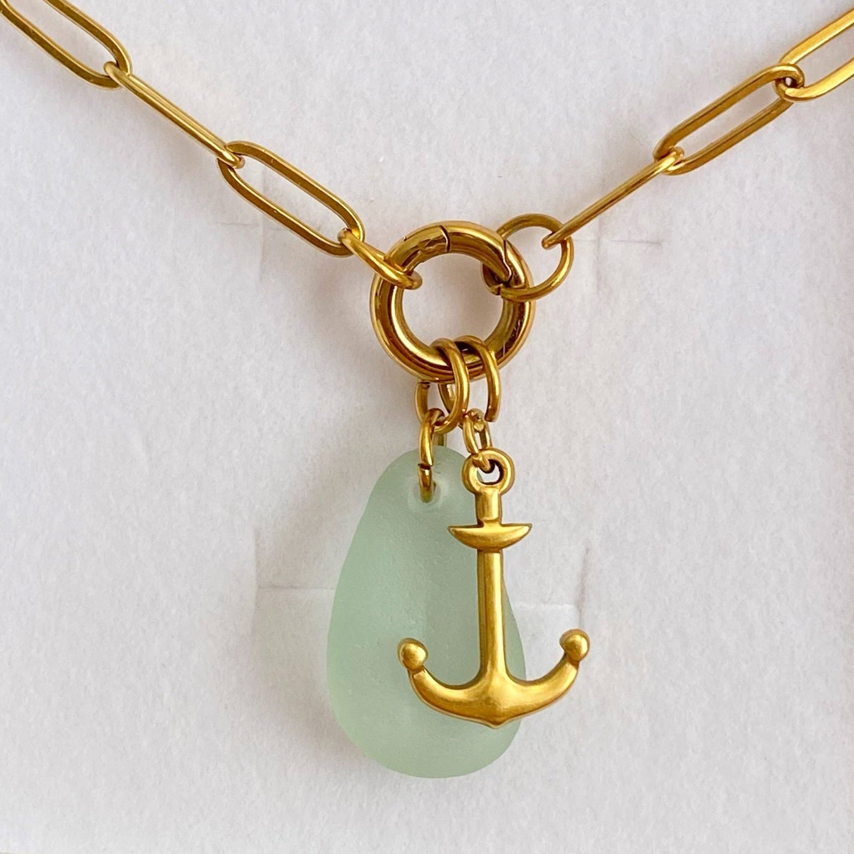 Gold necklace with a green teardrop pendant featuring an anchor design, displayed in a box.
