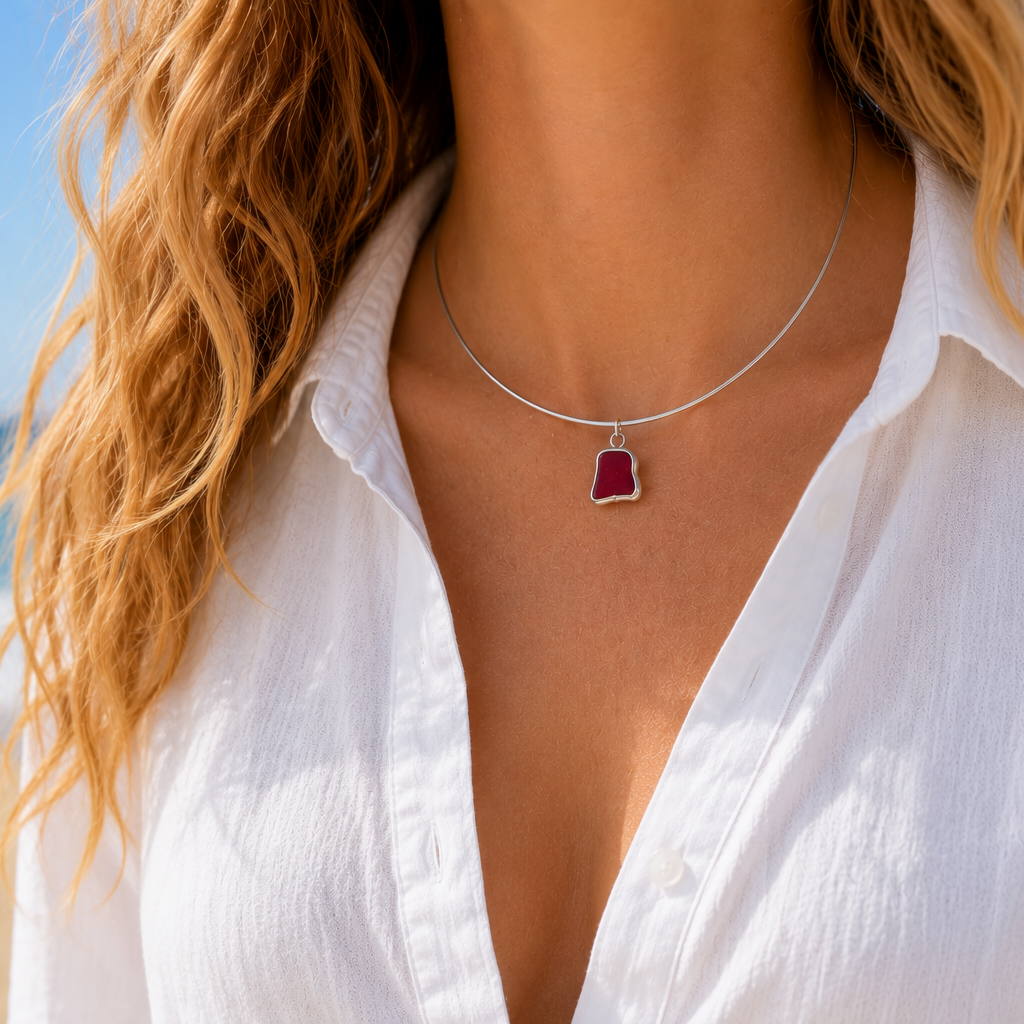 Person wearing a white shirt with a collar necklace with rare  red pendant on a beach.